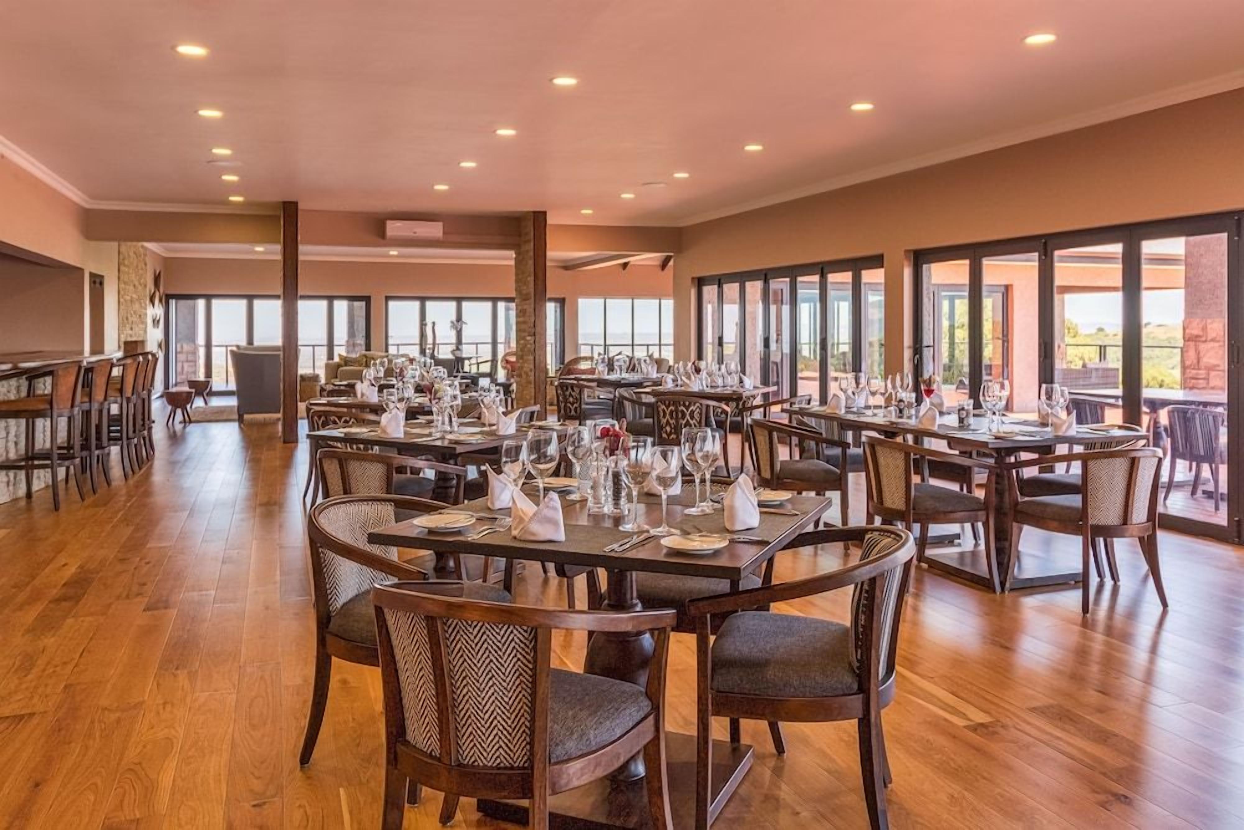 A spacious dining area with multiple tables and chairs, large windows, and a view of the outdoors.