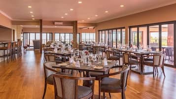 Un'ampia sala da pranzo con diversi tavoli e sedie, grandi finestre e vista sull'esterno.