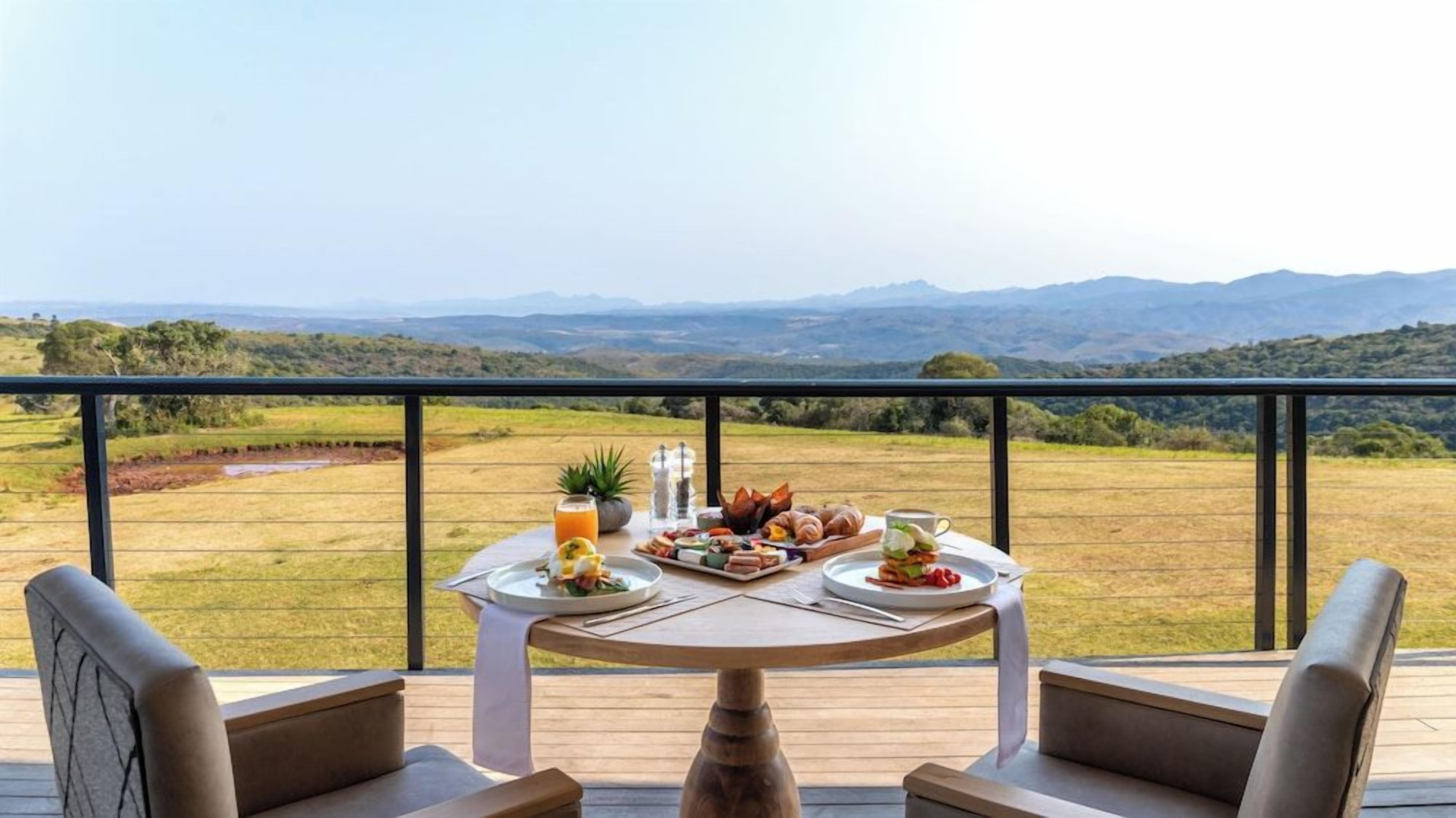 A dining table with breakfast items on a balcony overlooking a landscape with mountains.