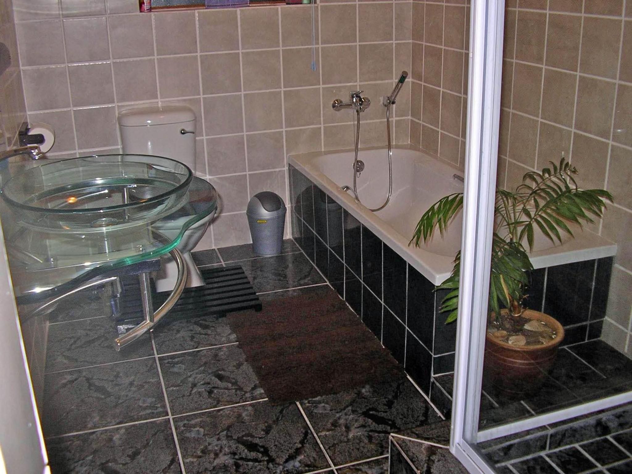 A bathroom with a glass bowl sink, a bathtub, a potted plant, and a shower area.