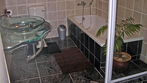 Een badkamer met een glazen wastafel, een bad, een potplant en een douchegedeelte.