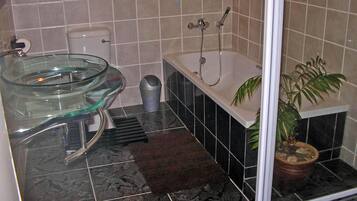 A bathroom with a glass bowl sink, a bathtub, a potted plant, and a shower area.