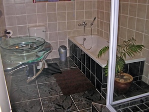 A bathroom with a glass bowl sink, a bathtub, a potted plant, and a shower area. - Little Lotta Cottage (Caledon)