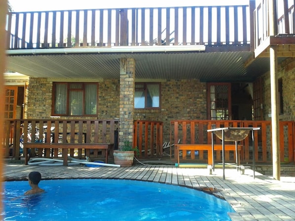 A pool area with a wooden deck, a stone building, and a metal roof structure. - Little Lotta Cottage (Caledon)
