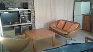 Een woonkamer met een bank, een salontafel, een televisie en een koelkast.
