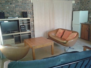 A living room with a sofa, a coffee table, a television, and a refrigerator. - Little Lotta Cottage (Caledon)