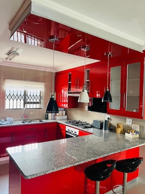 Cozinha moderna com armários vermelhos, bancada de granito, fogão a gás e dois banquetes pretos.