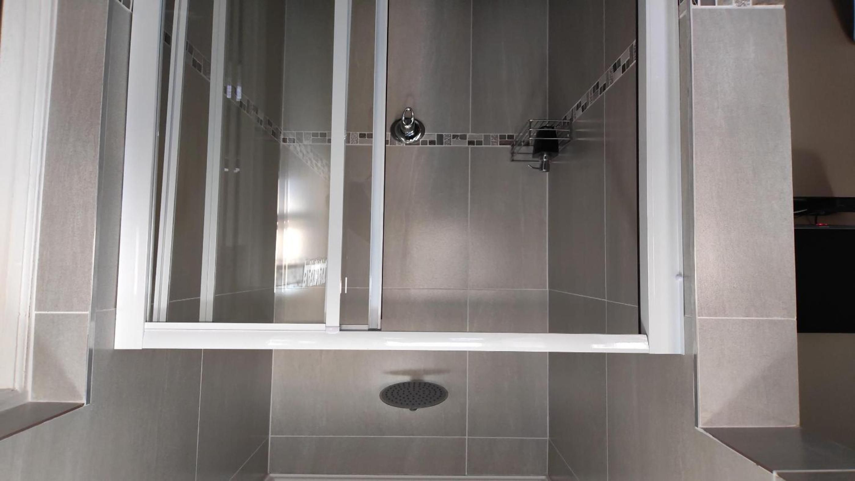 A modern shower enclosure with a glass door, a showerhead, and a drain.