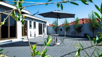 An outdoor patio area with a table and chairs, a large umbrella, and a building with windows and a door.