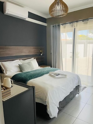 Quarto de hotel moderno com uma cama, mesa de cabeceira, abajur e vista para o exterior através de uma porta de vidro deslizante.