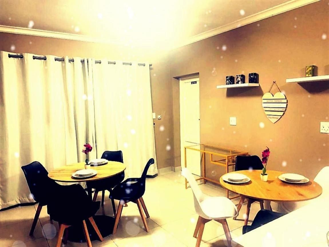 A dining area with a wooden table and chairs, a small side table with a vase, and a wall-mounted shelf with decorative items.