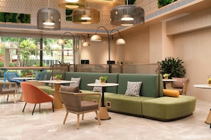 A modern interior with a green sofa, round tables, and chairs, and a large window offering a view of greenery. - Hilton Huiting Xishuangbanna Jinghong (Xishuangbanna Dai)