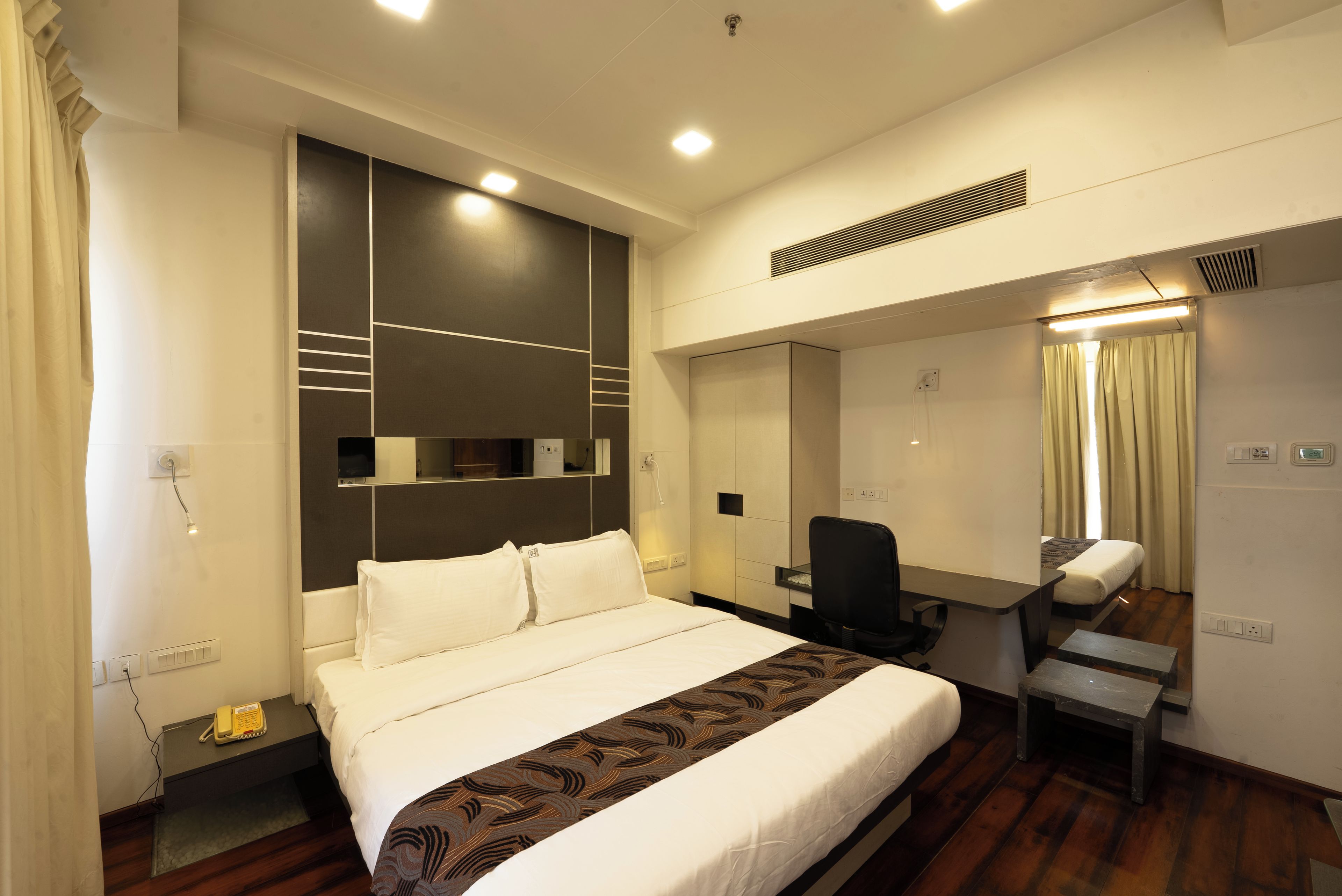 A hotel room with a large bed, a desk, a chair, a mirror, and a bathroom with a shower.