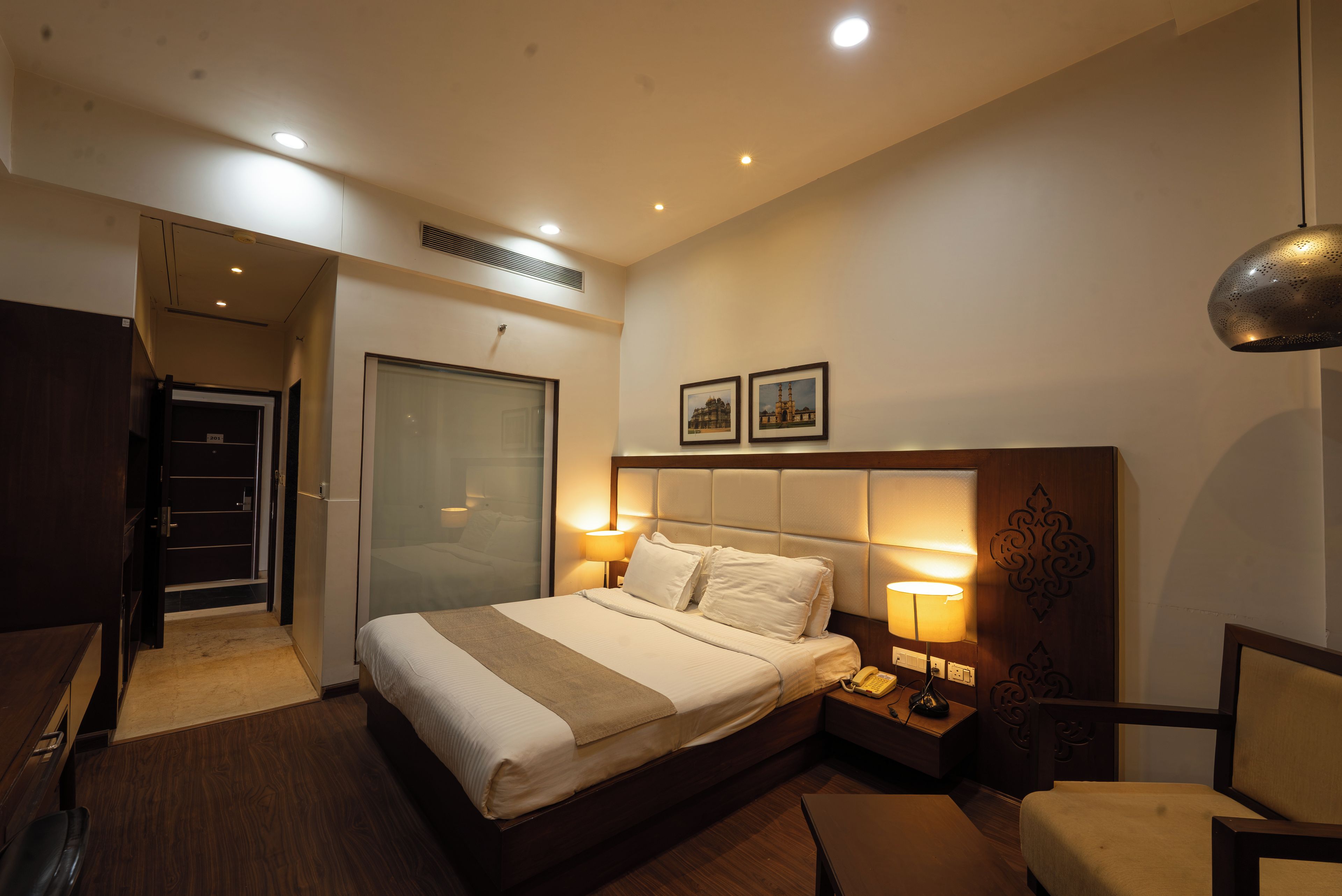 Quarto de hotel com cama, abajures, telefone, poltrona e armário.