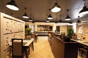 A modern restaurant interior with pendant lighting, wooden furniture, and a central serving area. - Manish Aura Grand (Vadodara)