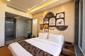 A hotel room with a bed, a glass shower enclosure, and wall art.