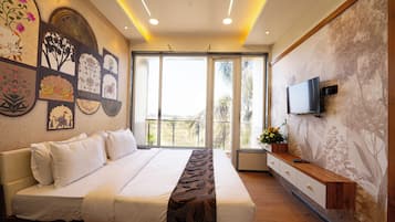 Habitación de hotel con una cama grande, un televisor de pantalla plana en la pared y un balcón con vistas a palmeras.