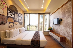 A hotel room with a large bed, a flat-screen TV mounted on the wall, and a balcony with a view of palm trees.