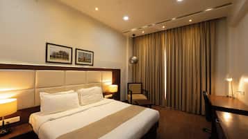 A hotel room with a large bed, a desk, a chair, and two framed pictures on the wall.