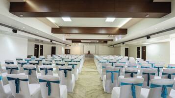 Un salón de conferencias con hileras de sillas blancas atadas con cintas azules, suelo de mármol y techo de madera con iluminación empotrada.