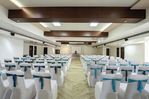 A conference room with rows of white chairs tied with blue sashes, a marble floor, and a wooden ceiling with recessed lighting. - Manish Aura Grand (Vadodara)