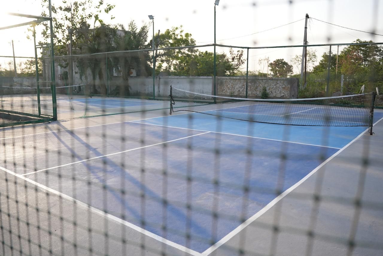 Een buitenbaan voor tennis met een net, omringd door een hek en bomen op de achtergrond.