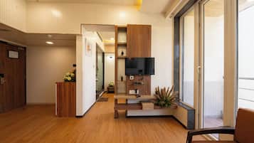 Un interior moderno con suelo de madera, un televisor de pantalla plana montado en un panel de madera, una mesita de madera con un jarrón de flores y un ventanal con vistas.