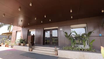 A building entrance with a modern design, featuring a set of steps leading to a glass door, potted plants, and a clear sky visible through the windows.