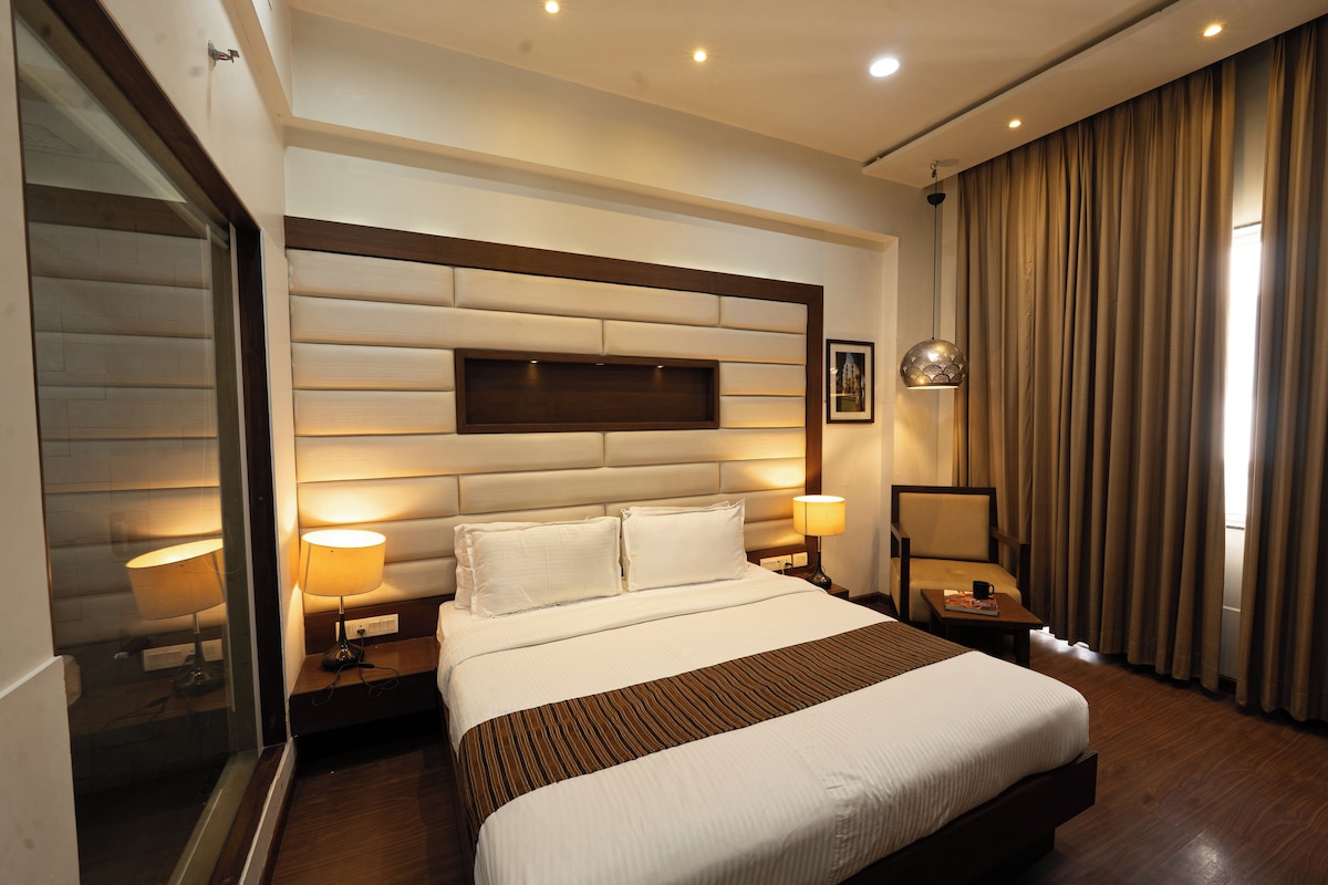 Ein Hotelzimmer mit einem großen Bett, zwei Nachttischlampen, einem Nachttisch, einem Fenster mit Vorhängen und einem Wandbild.