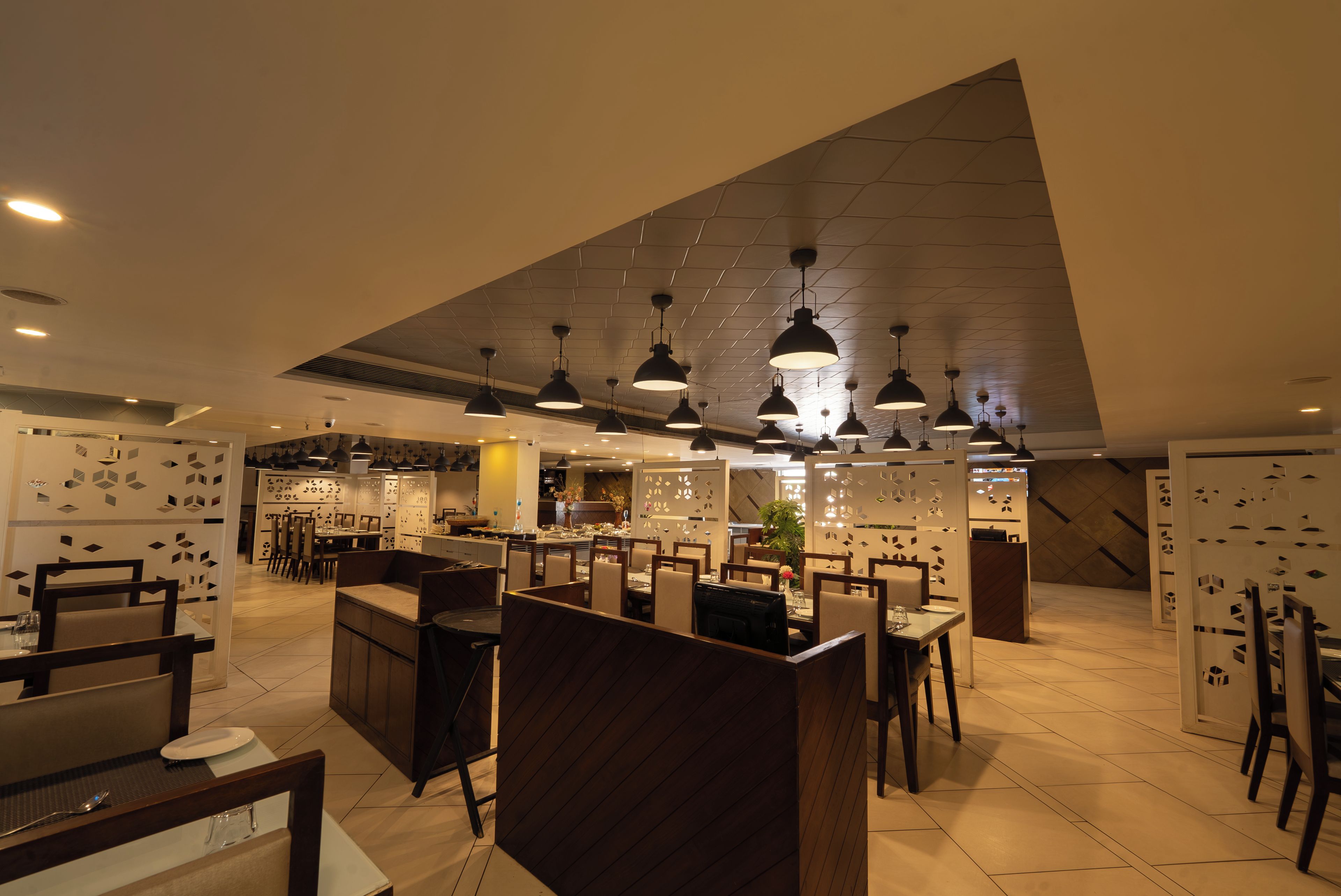 Un interior de restaurante moderno con techos altos, iluminación colgante y una combinación de asientos en cabinas y mesas.