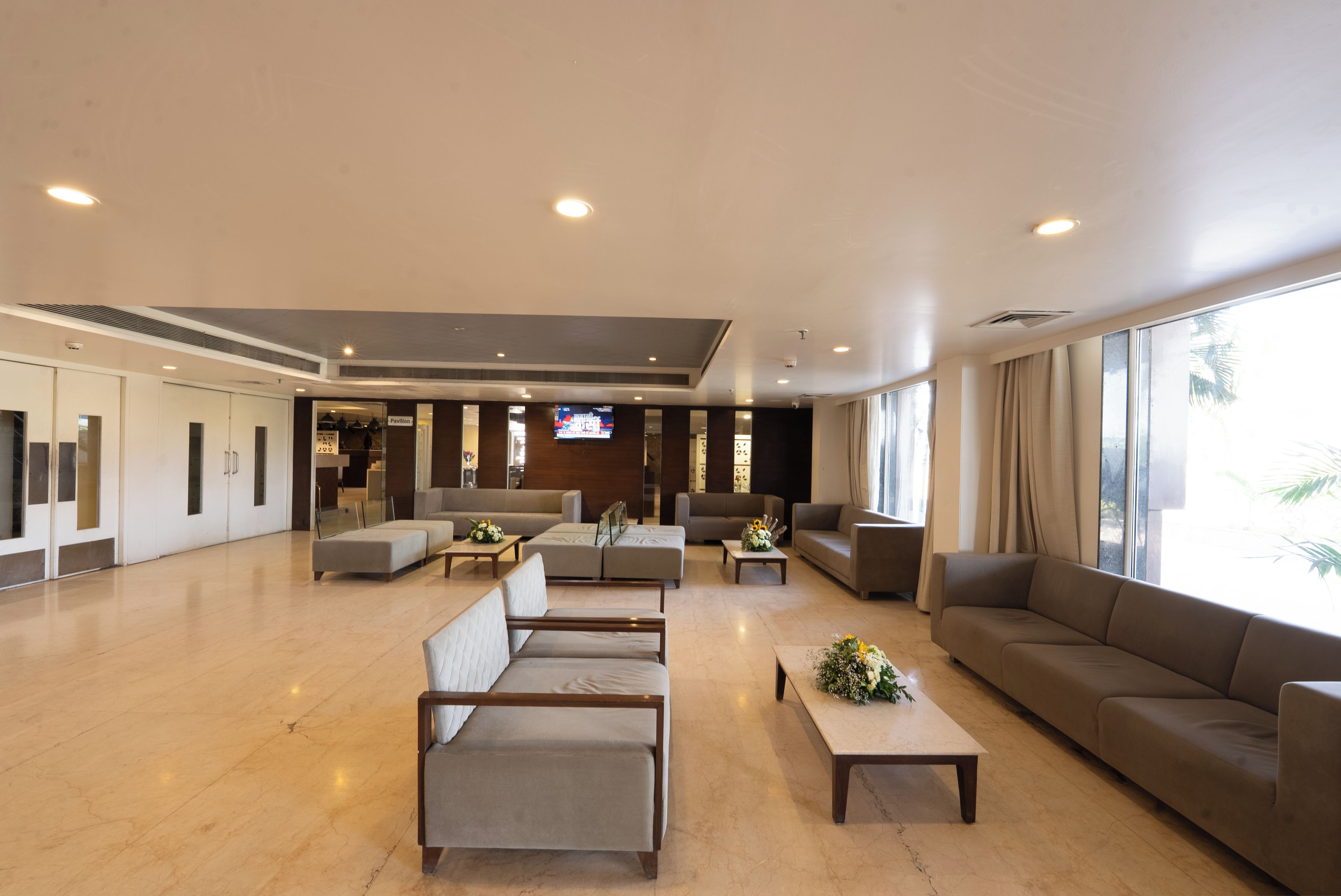Un vestíbulo amplio con diseño moderno, que cuenta con una zona de estar con sofás y sillones, un televisor montado en la pared y grandes ventanales que permiten la entrada de luz natural.