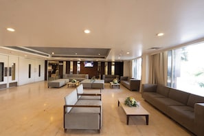 Eine geräumige Lobby im modernen Stil, mit einer Sitzecke, Sofas und Sesseln, einem an der Wand montierten Fernseher und großen Fenstern für viel Tageslicht.