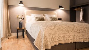 Een slaapkamer met een bed, nachtlampen, een nachtkastje, een kapstok en een houten vloer.