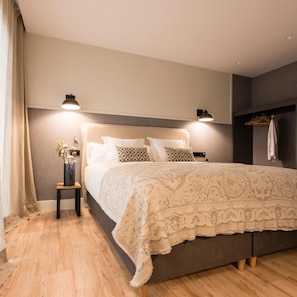 A bedroom with a bed, bedside lamps, a nightstand, a hanging coat rack, and a wooden floor. - Hotel Restaurante Rias Altas (Barreiros)