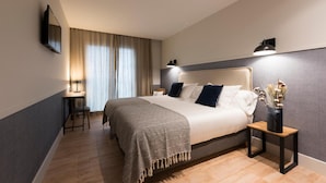 Een moderne hotelkamer met een groot bed, nachtlampjes, een bureau en een nachtkastje met een vaas gedroogde bloemen.