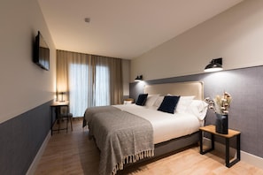 A modern hotel room with a large bed, bedside lamps, a desk, and a nightstand with a vase of dried flowers. - Hotel Restaurante Rias Altas (Barreiros)