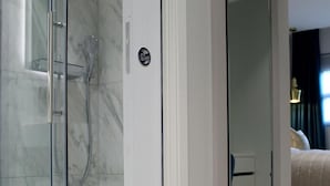A modern bathroom with a glass-enclosed shower, a marble-tiled wall, and a visible door handle. - NOX Waterloo (London)