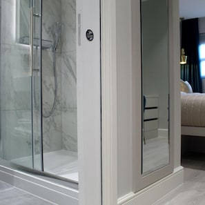 A modern bathroom with a glass-enclosed shower, a marble-tiled wall, and a visible door handle. - NOX Waterloo (London)