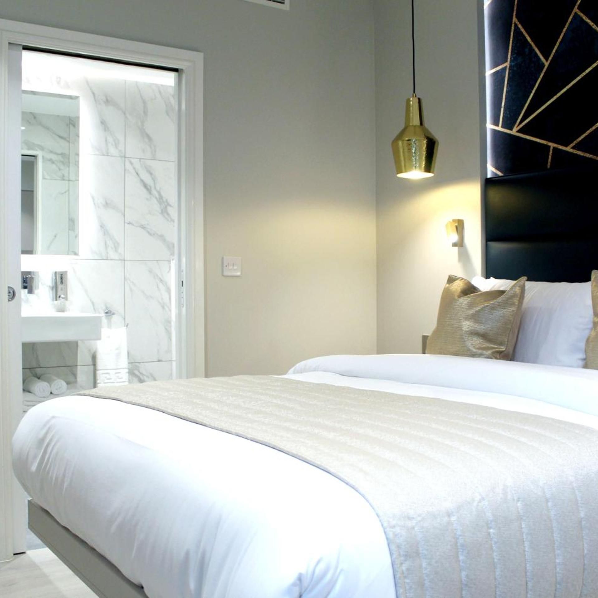 A hotel room with a large bed, a bathroom with a marble vanity, and a modern pendant light.