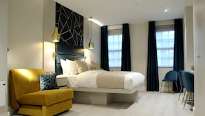 A modern bedroom with a bed, a yellow armchair, a desk, and a chair. - NOX Waterloo (London)