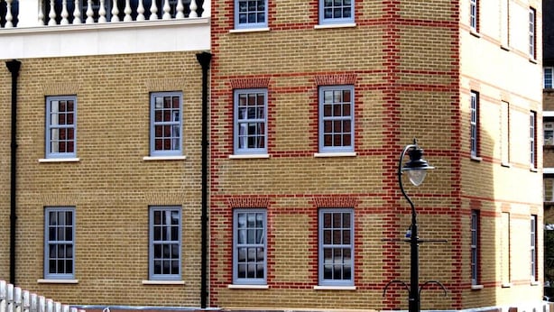 A multi-story building with a brick facade, multiple windows, and a white fence in the foreground. - NOX Waterloo (London)