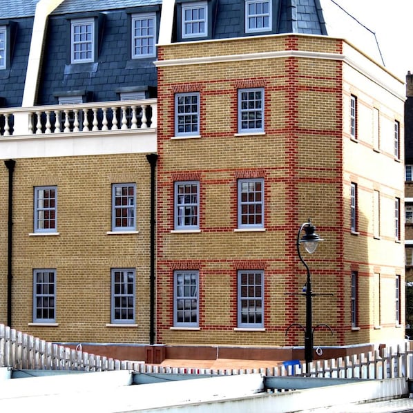 A multi-story building with a brick facade, multiple windows, and a white fence in the foreground. - NOX Waterloo (London)