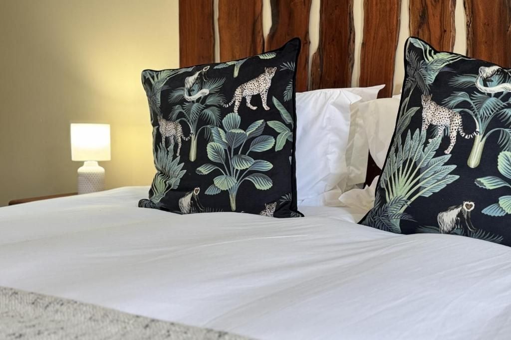 Una cama con ropa blanca y dos almohadas decorativas con motivos selváticos.
