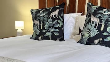 Una cama con ropa blanca y dos almohadas decorativas con motivos selváticos.