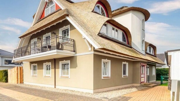 Een twee verdiepingen tellend huis met een balkon, rieten dak en een kleine garage.