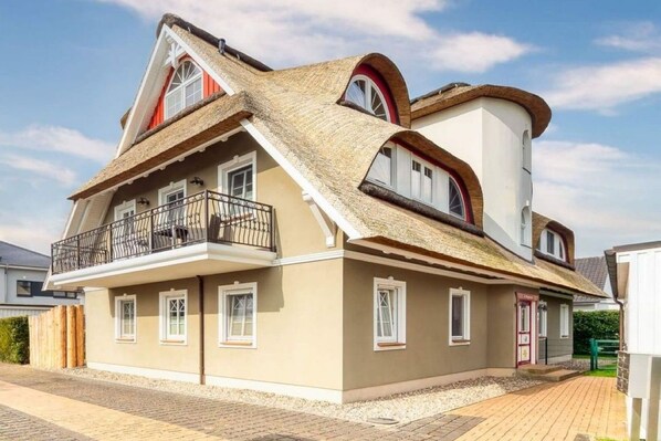 Een twee verdiepingen tellend huis met een balkon, rieten dak en een kleine garage.