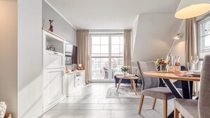 Een moderne keuken met witte kasten, een eethoek met een ronde tafel en uitzicht door een groot raam.