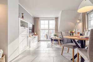 Een moderne keuken met witte kasten, een eethoek met een ronde tafel en uitzicht door een groot raam.