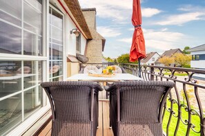 Een balkon met rieten meubilair, een tafel met fruit en bloemen, en een rode parasol.
