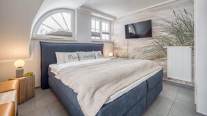 Een slaapkamer met een bed, bedlampen, een televisie en een raam.